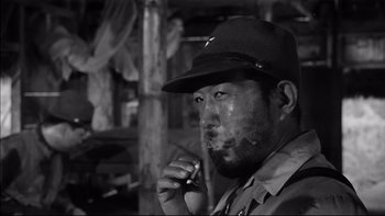 Movie still from “King Rat” (1965), directed by Bryan Forbes – A black and white photo of a man smoking a cigarette; Close Up shot, Low angle