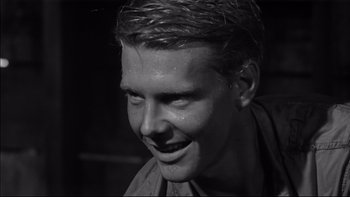 Movie still from “King Rat” (1965), directed by Bryan Forbes – A young man with wet hair smiling for the camera; Close Up shot, Over the shoulder angle