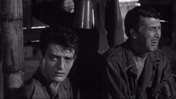 Movie still from “King Rat” (1965), directed by Bryan Forbes – A man with a wet shirt on and another man with a mug in the background; Close Up shot, Low angle