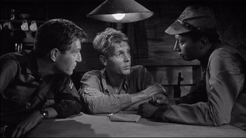 Movie still from “King Rat” (1965), directed by Bryan Forbes – A group of men sitting at a table with a lamp above them; Close Up shot, Over the shoulder angle