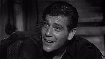 Movie still from “King Rat” (1965), directed by Bryan Forbes – Black and white photograph of a man smiling for the camera; Close Up shot, Low angle