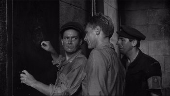 Movie still from “King Rat” (1965), directed by Bryan Forbes – A group of men standing next to each other near a wall; Medium shot, Over the shoulder angle