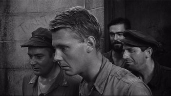 Movie still from “King Rat” (1965), directed by Bryan Forbes – Black and white photograph of a man in front of a group of men; Close Up shot, Low angle