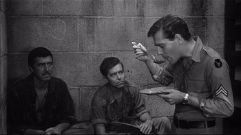 Movie still from “King Rat” (1965), directed by Bryan Forbes – A black - and - white photo of three men sitting on the ground; Medium shot, High angle