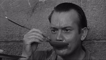 Movie still from “King Rat” (1965), directed by Bryan Forbes – A black and white photo of a man with a spoon in his mouth; Close Up shot, High angle