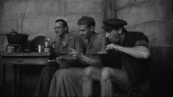 Movie still from “King Rat” (1965), directed by Bryan Forbes – A group of men sitting next to each other eating food; Medium shot, High angle