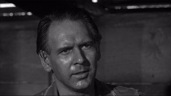 Movie still from “King Rat” (1965), directed by Bryan Forbes – Black and white photograph of a man with a wet face; Close Up shot, Over the shoulder angle