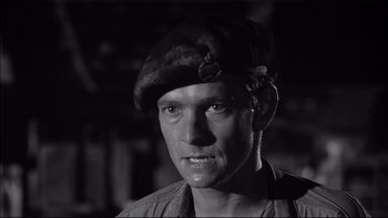 Movie still from “King Rat” (1965), directed by Bryan Forbes – A black and white photo of a man wearing a hat; Close Up shot, Over the shoulder angle