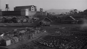 Movie still from “King Rat” (1965), directed by Bryan Forbes – A black and white photo of a village with buildings; Extreme Wide shot, High angle