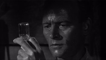 Movie still from “King Rat” (1965), directed by Bryan Forbes – A black and white photo of a man holding a glass of water; Close Up shot, High angle