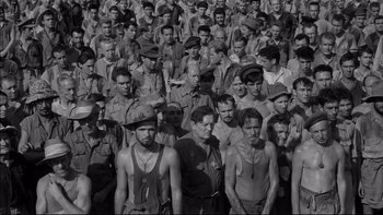 Movie still from “King Rat” (1965), directed by Bryan Forbes – A large group of men standing together in a field; Wide shot, High angle