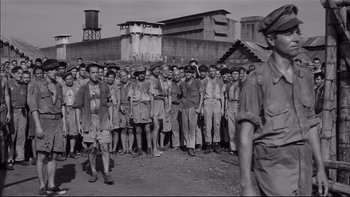 Movie still from “King Rat” (1965), directed by Bryan Forbes – A group of men standing next to each other in front of a building; Wide shot, High angle
