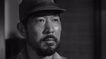 Movie still from “King Rat” (1965), directed by Bryan Forbes – Black and white photograph of a man wearing a hat; Close Up shot, Low angle