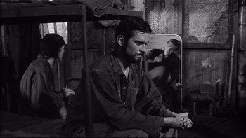 Movie still from “King Rat” (1965), directed by Bryan Forbes – A black and white photo of a man sitting in a chair; Medium shot, Over the shoulder angle