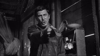 Movie still from “King Rat” (1965), directed by Bryan Forbes – A black - and - white photo of a man holding something in his hand; Medium shot, Low angle