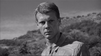 Movie still from “King Rat” (1965), directed by Bryan Forbes – Black and white photograph of a young man in a field; Close Up shot, Low angle