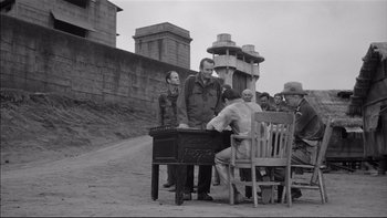 Movie still from “King Rat” (1965), directed by Bryan Forbes – A group of people sitting around a table; Wide shot, Over the shoulder angle