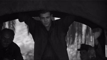 Movie still from “King Rat” (1965), directed by Bryan Forbes – A black and white photo of a man holding an umbrella; Medium shot, Low angle