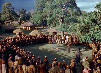 Movie still from “King Solomon's Mines” (1950), directed by Andrew Marton – A group of people sitting in a circle in front of a crowd; Extreme Wide shot, High angle