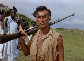 Movie still from “King Solomon's Mines” (1950), directed by Andrew Marton – A man holding a rifle while standing in a field; Close Up shot, Low angle