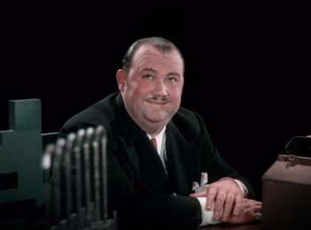 Movie still from “King of Jazz” (1930), directed by Walter Lantz – An older man sitting at a table in front of a black background; Close Up shot, High angle