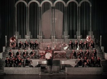Movie still from “King of Jazz” (1930), directed by Walter Lantz – A group of people in a large room with a band playing instruments; Extreme Wide shot, High angle