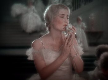 Movie still from “King of Jazz” (1930), directed by Walter Lantz – A woman in a white dress is holding a glass; Close Up shot, High angle