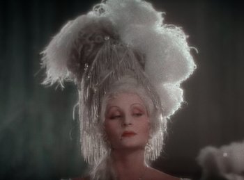 Movie still from “King of Jazz” (1930), directed by Walter Lantz – A woman in a white dress with a white feather hat on her head; Close Up shot, Low angle