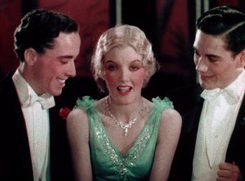 Movie still from “King of Jazz” (1930), directed by Walter Lantz – A group of men standing next to a woman in a green dress; Medium shot, High angle