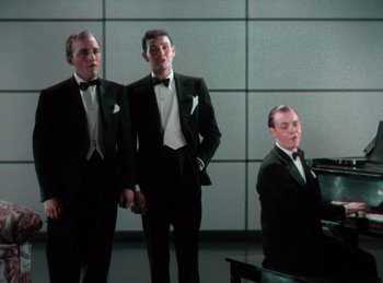 Movie still from “King of Jazz” (1930), directed by Walter Lantz – Three men in tuxedos standing in front of a piano; Medium shot, Low angle