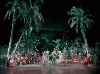 Movie still from “King of Jazz” (1930), directed by Walter Lantz – A group of people are dancing on a stage in front of palm trees; Extreme Wide shot, High angle