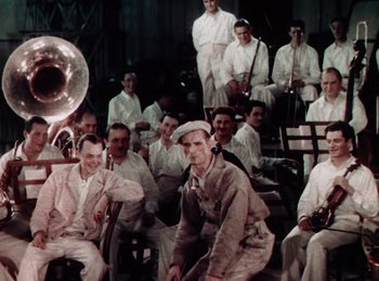 Movie still from “King of Jazz” (1930), directed by Walter Lantz – A group of men sitting and standing around each other; Wide shot, High angle