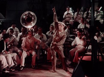 Movie still from “King of Jazz” (1930), directed by Walter Lantz – A group of men sitting in front of each other on a stage; Wide shot, High angle