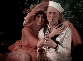 Movie still from “King of Jazz” (1930), directed by Walter Lantz – A man and a woman are posing with a saxophone; Medium shot, High angle