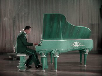 Movie still from “King of Jazz” (1930), directed by Walter Lantz – A man sitting at a green piano in a room; Wide shot, High angle
