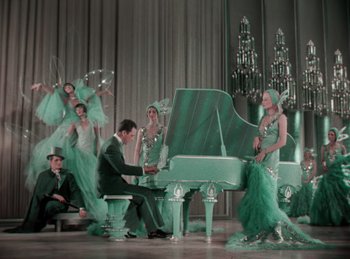 Movie still from “King of Jazz” (1930), directed by Walter Lantz – A group of people dressed up in costumes and playing a piano; Wide shot, High angle
