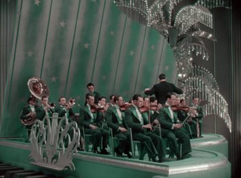 Movie still from “King of Jazz” (1930), directed by Walter Lantz – A group of men in green suits sitting on chairs; Extreme Wide shot, High angle