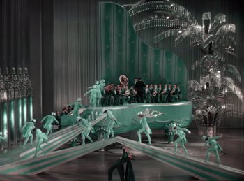 Movie still from “King of Jazz” (1930), directed by Walter Lantz – A group of people in green costumes performing on a stage; Extreme Wide shot, High angle