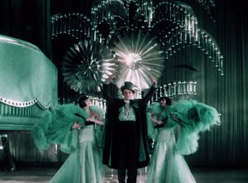 Movie still from “King of Jazz” (1930), directed by Walter Lantz – A man in a top hat holding an umbrella between two women; Wide shot, Low angle