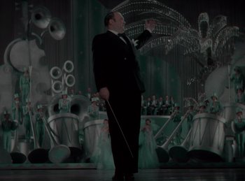 Movie still from “King of Jazz” (1930), directed by Walter Lantz – A man in a suit and tie holding a cane; Medium shot, Low angle