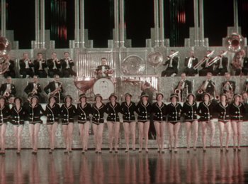 Movie still from “King of Jazz” (1930), directed by Walter Lantz – A group of women standing in front of an orchestra; Extreme Wide shot, High angle