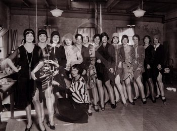 Movie still from “King of Jazz” (1930), directed by Walter Lantz – A group of women posing for a picture in a room; Wide shot, Low angle