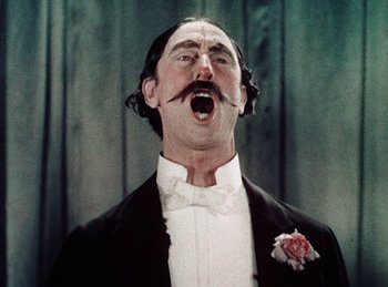 Movie still from “King of Jazz” (1930), directed by Walter Lantz – A man in a tuxedo with a mustache and a flower in his mouth; Close Up shot, Low angle