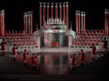 Movie still from “King of Jazz” (1930), directed by Walter Lantz – A group of men in red uniforms standing in front of a stage; Extreme Wide shot, High angle