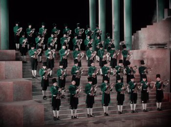 Movie still from “King of Jazz” (1930), directed by Walter Lantz – A group of men in green and black uniforms standing on steps; Extreme Wide shot, High angle