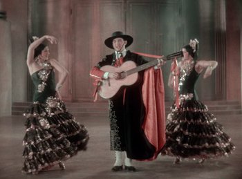 Movie still from “King of Jazz” (1930), directed by Walter Lantz – A man holding a guitar in front of two dancers; Wide shot, Low angle