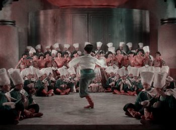 Movie still from “King of Jazz” (1930), directed by Walter Lantz – A group of people sitting and standing in a room; Extreme Wide shot, High angle