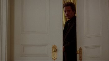 Movie still from “King of New York” (1990), directed by Abel Ferrara – A man standing in front of a white door; Medium shot, Over the shoulder angle