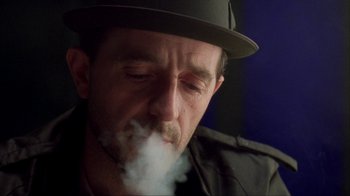 Movie still from “King of New York” (1990), directed by Abel Ferrara – A person with a hat smoking a cigarette; Close Up shot, Low angle