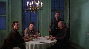 Movie still from “King of New York” (1990), directed by Abel Ferrara – A group of men sitting around a table; Wide shot, Low angle